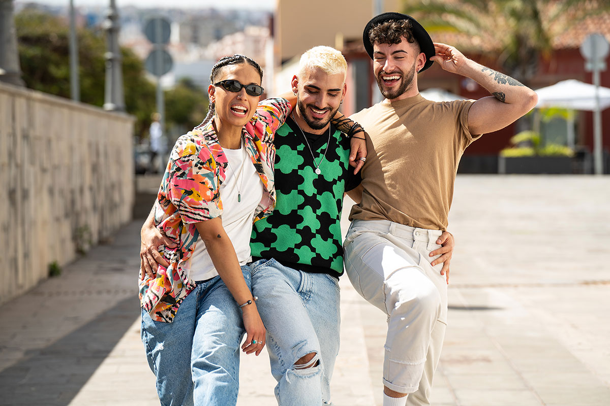 Three happy young people walking in the city, talking to each other, laughing and having fun. Multiethnic group of friends. Real people lifestyle.