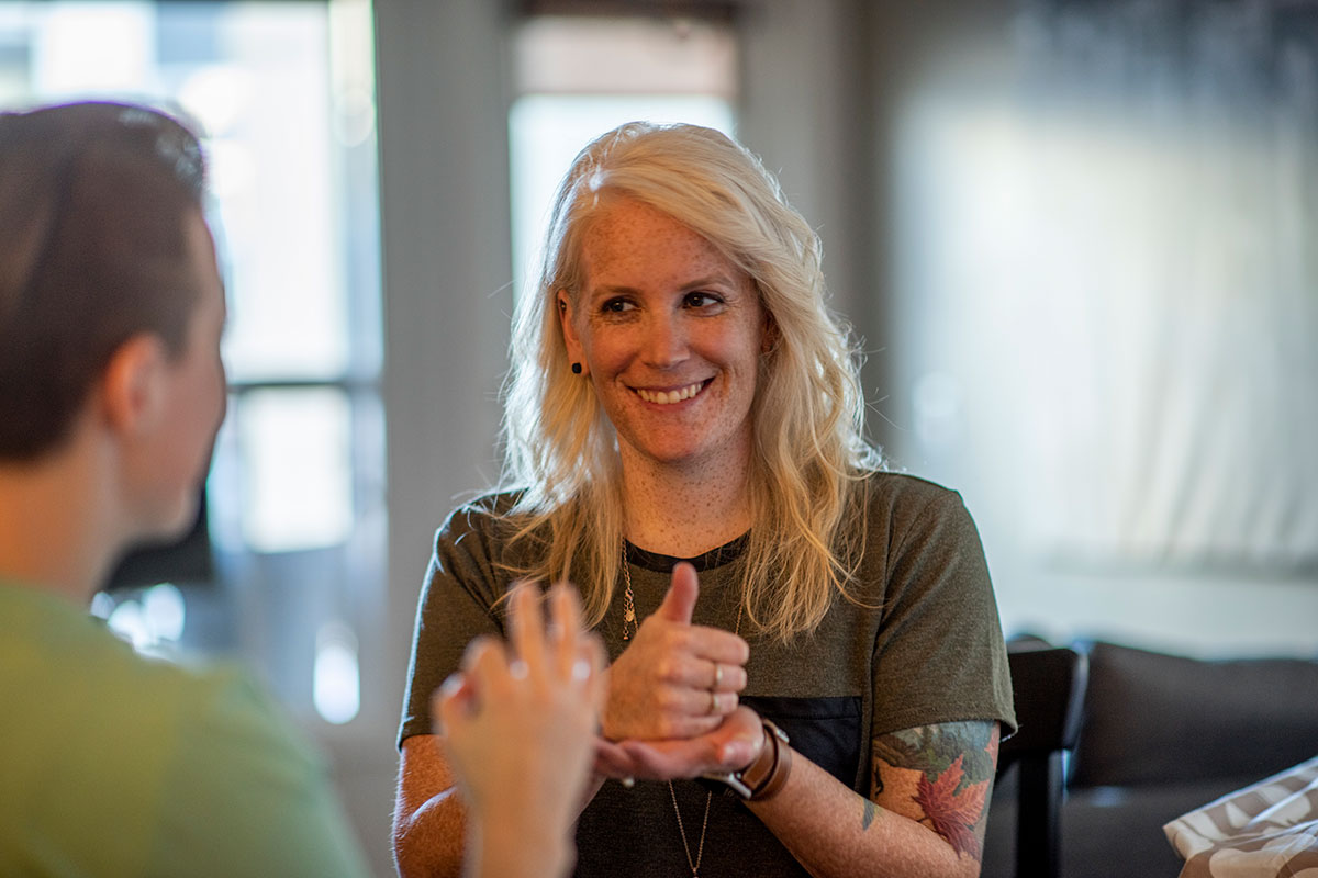 A deaf blonde woman communicates with her girlfriend through ASL one afternoon in their home.