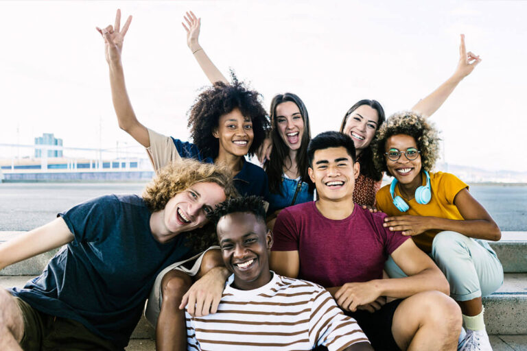 A diverse group of young adults smile and pose cheerfully together outdoors, radiating joy and friendship.